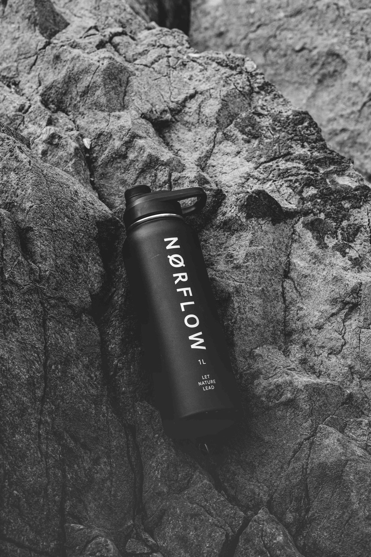 Botella térmica NORFLOW 1L de acero inoxidable apoyada en una roca, foto en blanco y negro