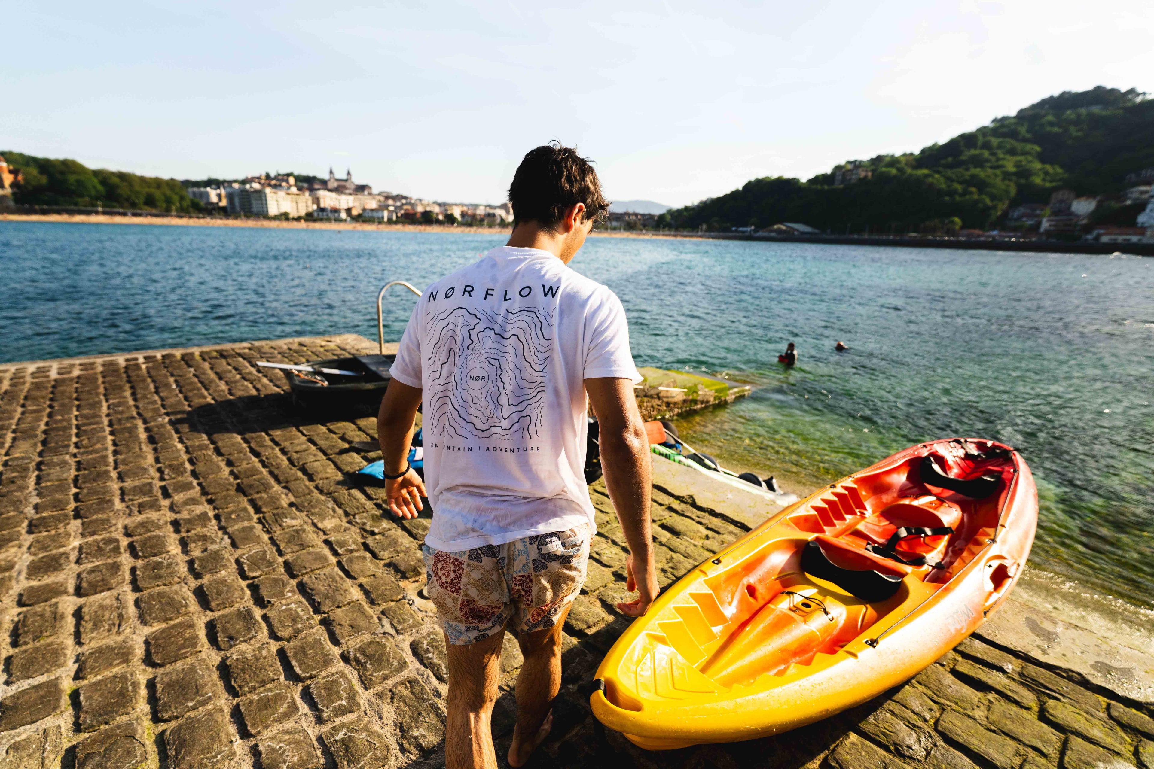 Modelo joven llevando la camiseta de la marca Norflow usando el Kayak en una isla. Camiseta preparada para la aventura, montaña y mar. Perfecta para usar el días de playa con el Kayak. 