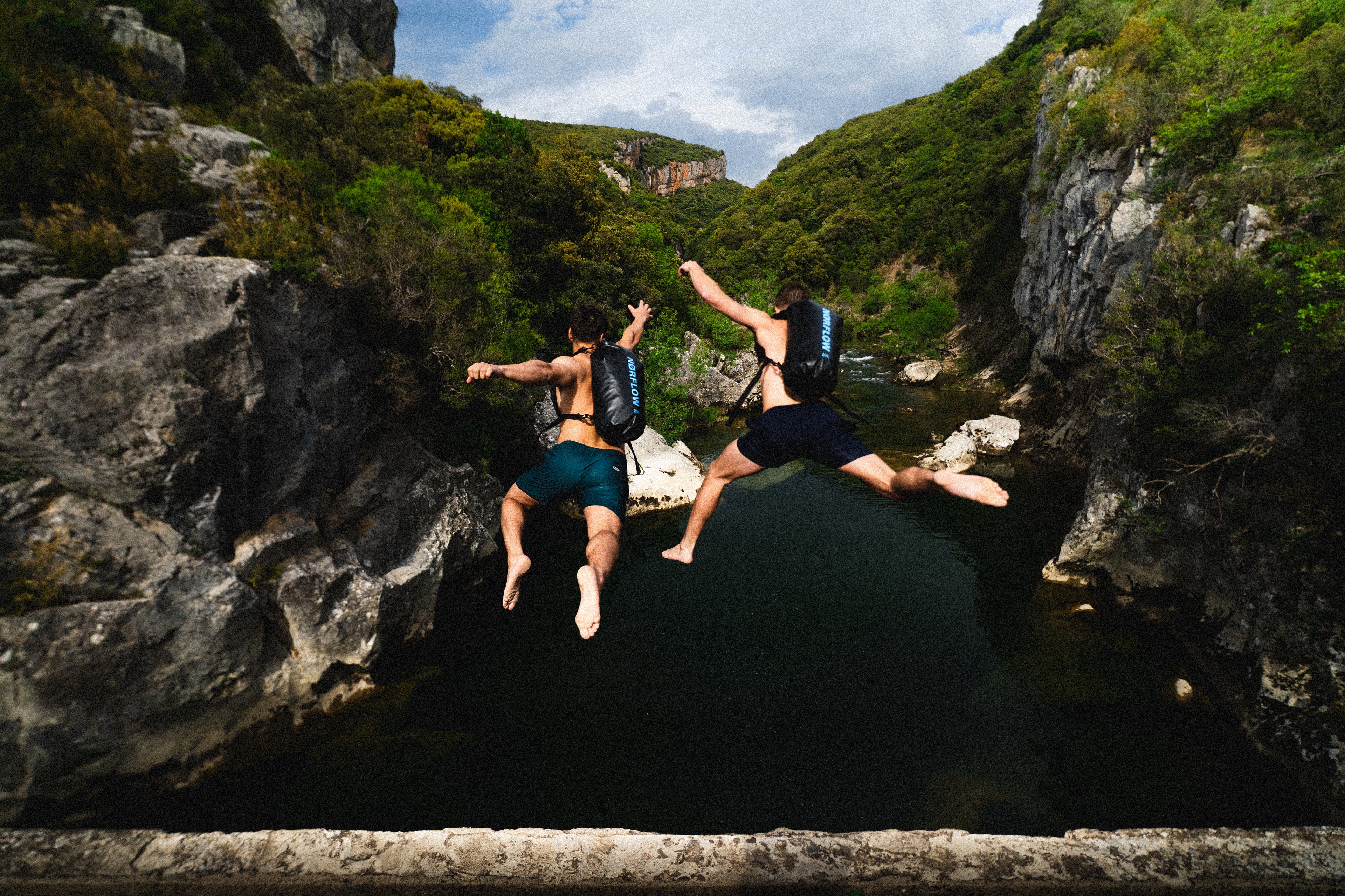 Dos jovenes en un puente sobre el río usando la mochila estanca de NØRFLOW de 20L con cierre hermético y correas ajustables, ideal para actividades al aire libre y deportes acuáticos. Marca inspirada en el mar, la montaña y la aventura. Norflow nace de la necesidad de explorar y descubrir nuevos lugares perdidos por el norte. Diseña productos funcionales para acompañar experiencias al aire libre, combinando utilidad, durabilidad y un estilo de vida activo.
