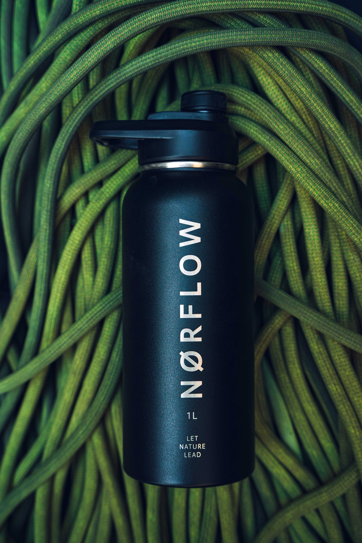 Botella térmica NORFLOW 1L negra sobre una cuerda de escalada verde enrollada